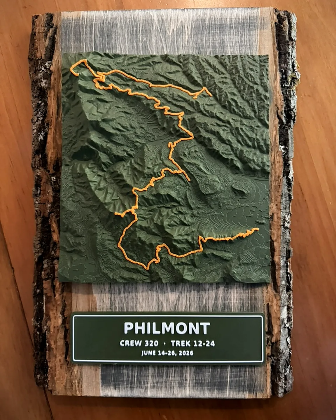 Olive green 3D terrain print with a raised orange route and a nameplate reading Philmont, Crew 320, mounted on a live-edge wood slab